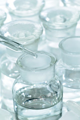 Dropper with chemical reagent being added to bottle on white background.