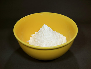 Pure white raw flour in yellow ceramic mixing bowl isolated on black background