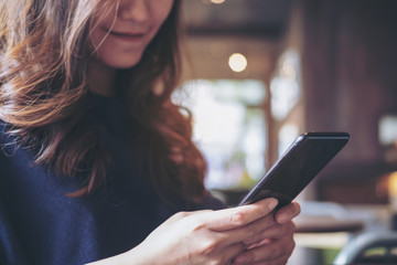 A beautiful Asian woman with smiley face using and looking at a black smart phone in modern loft cafe