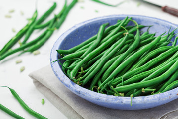 Crop of green or string beans in vintage blue bowl on white table. Organic and diet food.