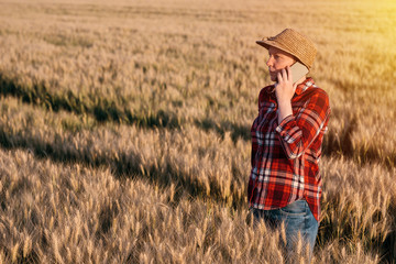 Naklejka na ściany i meble Female farmer in wheat field talking on mobile phone