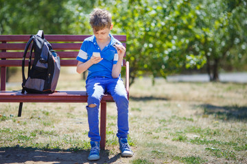 Schoolboy playing with fidget spinner and smartphone after classes. Entertainment, trendy toys,...