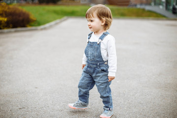 Fototapeta premium Cute baby girl with blonde hair running outdoors. Little girl 1-2 year old.