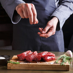 Chef seasoning filet mignon on wooden board at restaurant kitchen