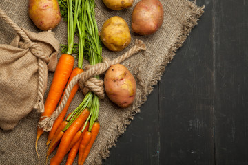 Fresh carrots and potatoes on a black wooden background. rustic style