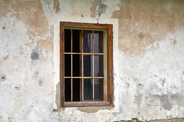 Fototapeta na wymiar Old rotten window with rusty iron bars, missing the outer moving frames, in a ruined house facade