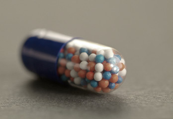 Transparent medicinal capsule with multi-colored balls on a gray background. Selective focus