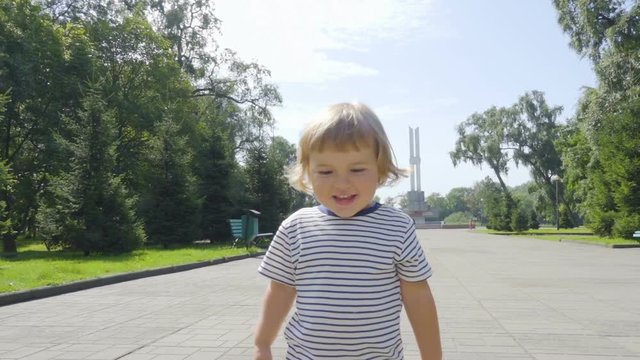 Little boy walking along the city street. Slow Motion. Happy child walk to the camera in the park outdoors.