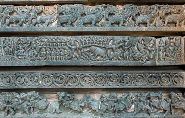 Hunting scene and other stone artworks on background sculptures on the Hindu temple. Mythical patterns of 12th century Hoysaleshwara temple in Halebidu, India