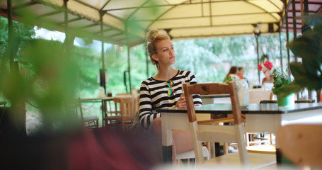 Fototapeta na wymiar Pretty young caucasian girl sitting at outdoors cafe and waiting for someone.