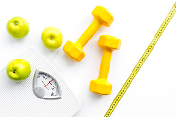 Sport and diet for losing weight. Bathroom scale, apple and dumbbell on white background top view