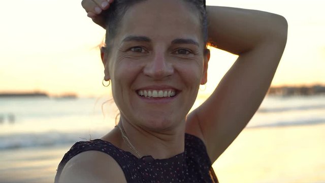 Beautiful woman smiling to the camera while standing on the beach during sunset, steadycam shot
