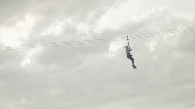 Man riding zip line in mountains at height of several metres with grey sky behind
