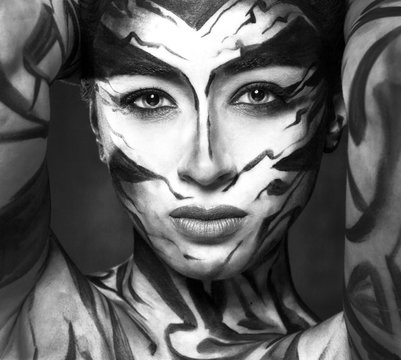 A beautiful woman with face art looks at us intently.
