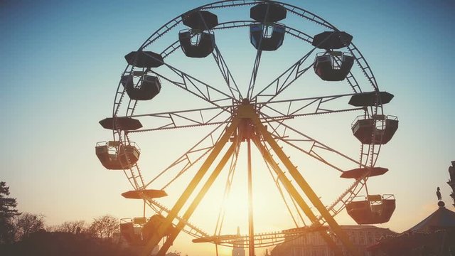 Children's Ferris wheel with cabs and umbrellas slowly rotating. Sunset sky in the background. Vintage toning filter. Childhood, entertainment, holidays concept. Mikhaylovskaya square, Kiev, Ukraine