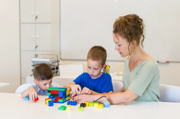 Obraz premium teacher woman play with two child boy with cubes in the kindergarten