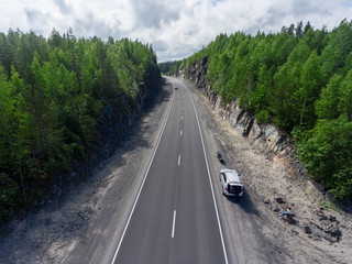 Passenger car and motorcycle standing on roadside of country two lane highway between rocks, aerial view