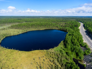 Fototapeta premium Aerial view at small forest lake, swamps and line of highway passing near. Northern Karelia, Russia