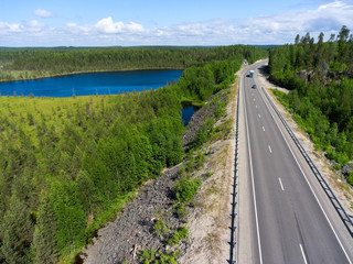 Aerial view at the country highway passing near forest lake in evergreen northern forests