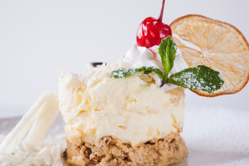 Creamy orange dessert serving on white background in restaurant. Delicious cake decorated by dried citrus, cherry and mint, real pleasure of sweets. Close up picture