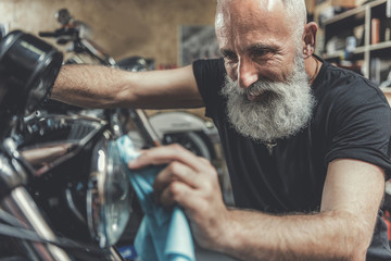 Happy smiling old man cleaning motorbike