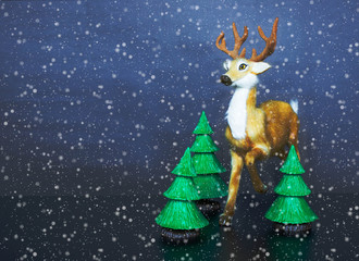 Christmas toy deer with wicker sled, fir branches and new year tree ball on dark blue or black background. Snowfall overlay on holiday decorative installation.