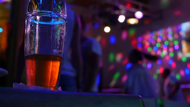 Not finishing a mug with beer on the table in the disco bar against the background of dancing people. 4k.