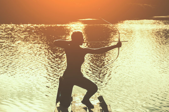The silhouette of the athlete is aimed at the target and shoots an arrow on the background of the lake. Archery.