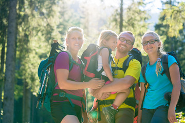 Family with two daughters on hike in the woods backlit in summer
