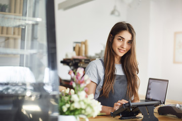 Coffee shop owner using a tablet looking at camera smiling, ready for her first customer