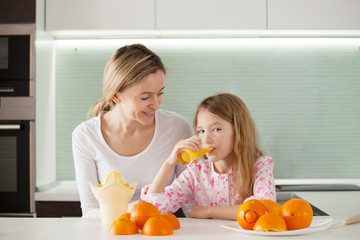 Mother and daughter make orange juice on a juicer