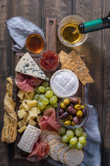 Cheese plate served with grapes, jam, prosciutto and crackers on a wooden background