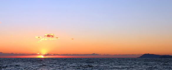 sunset behind clouds at the horizon over the sea