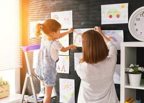Mother and child girl hang their drawings on wall