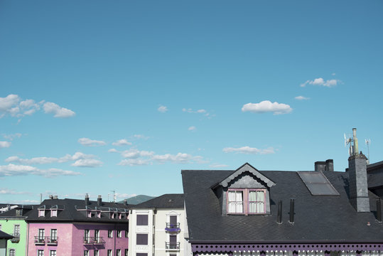 Tejados de casas en un pueblo con fachadas de colores. Bajo un cielo azul con nubes.