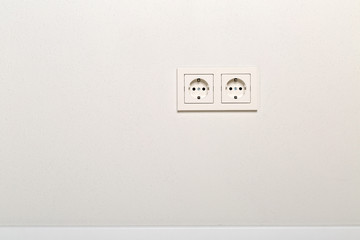 Empty, unplugged european wall outlet on white plaster wall