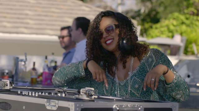 Young dark-skinned woman wearing sunglasses, having fun and spinning disks for an outdoor party at a resort location. Slow motion 4K, shot at 60fps.