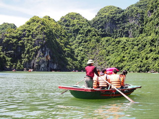 Tourist bamboo boat tour in Ha long bay sea with continuous cliffs in Vietnam