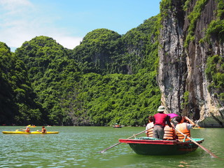 Tourist bamboo boats and kayaks with high green tree forest cliffs in Ha long bay, Vietnam