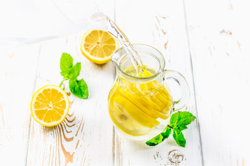 In a jug of lemons pour water on a white wooden background.
