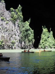 Kayaks on the green sea beside the cliff, with the stalactite stone silhouette  