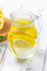A pitcher with a cold lemonade on a white wooden background surrounded by lemons.