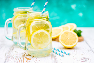 Banks with handles with cold lemonade on a white wooden background. Lemons.