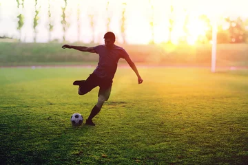 Foto auf Acrylglas Fußballspieler schießt bei Sonnenuntergang einen Ball im Stadion. © vchalup
