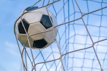 Goal - soccer or football ball in the net against blue sky.