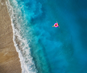 Aerial view of young woman swimming on the pink swim ring in the transparent turquoise sea in...