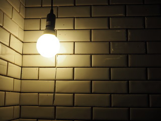 Yellow hanging light bulb lamp and ceramic tile brick corner wall, dark background