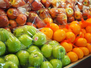 Green and red apple, orange packed in transparent plastic bag, in fruit market stall
