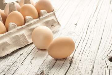 chicken eggs in cardboard box on white wooden background