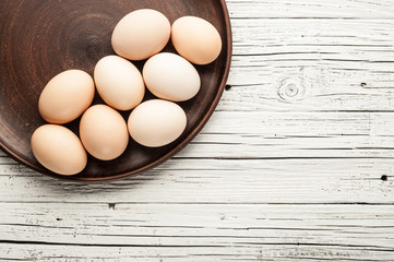 chicken eggs in clay plate on white wooden background